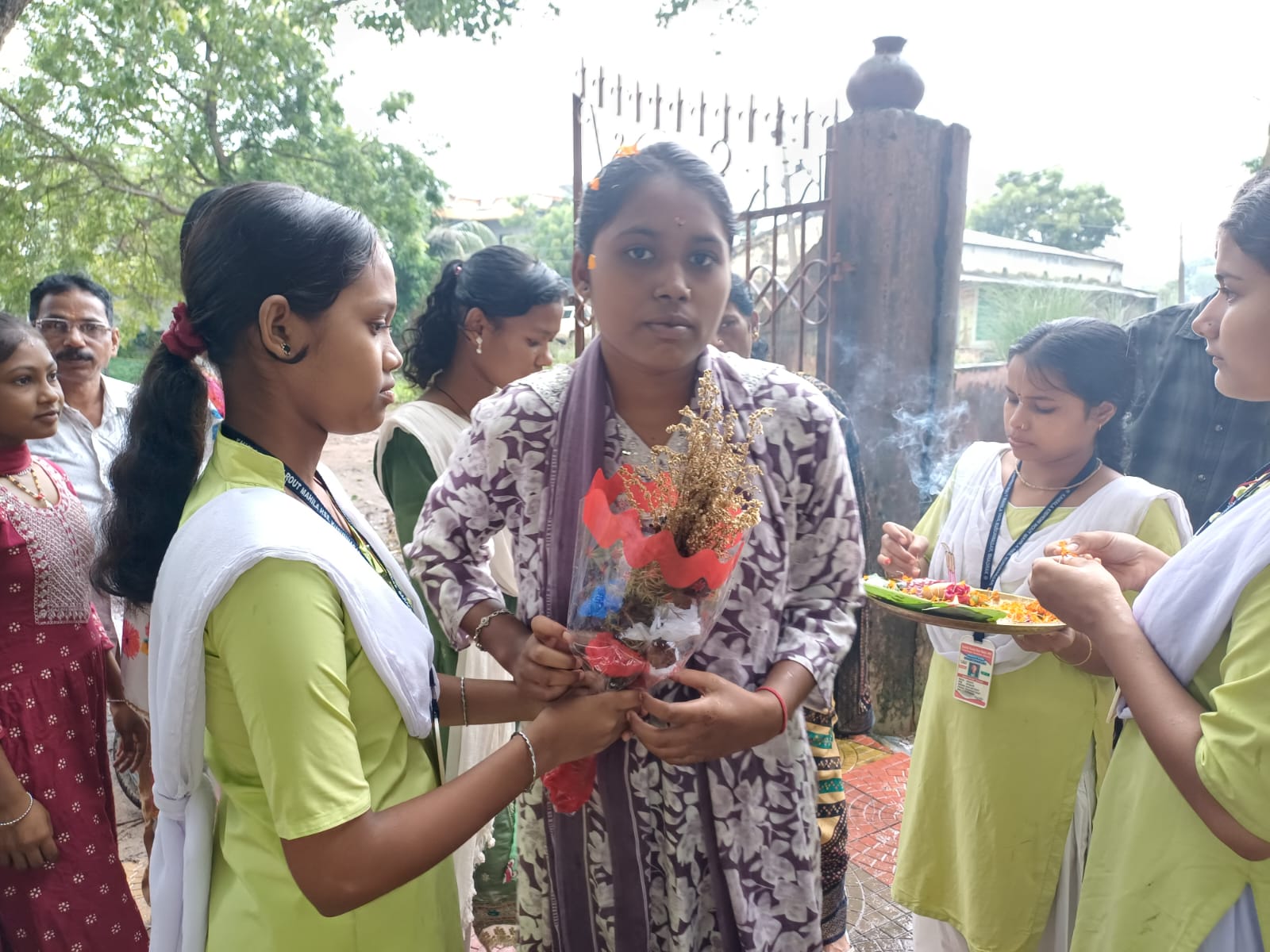 Students in uniform welcoming a guest with flowers and a ceremonial thali on the school campus