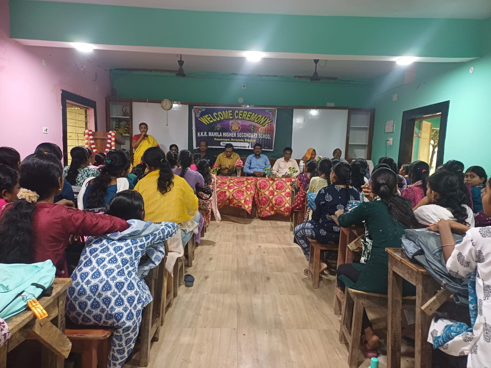 Welcome ceremony at KKR Mahila Higher Secondary School with guests at the head table and students seated in the hall